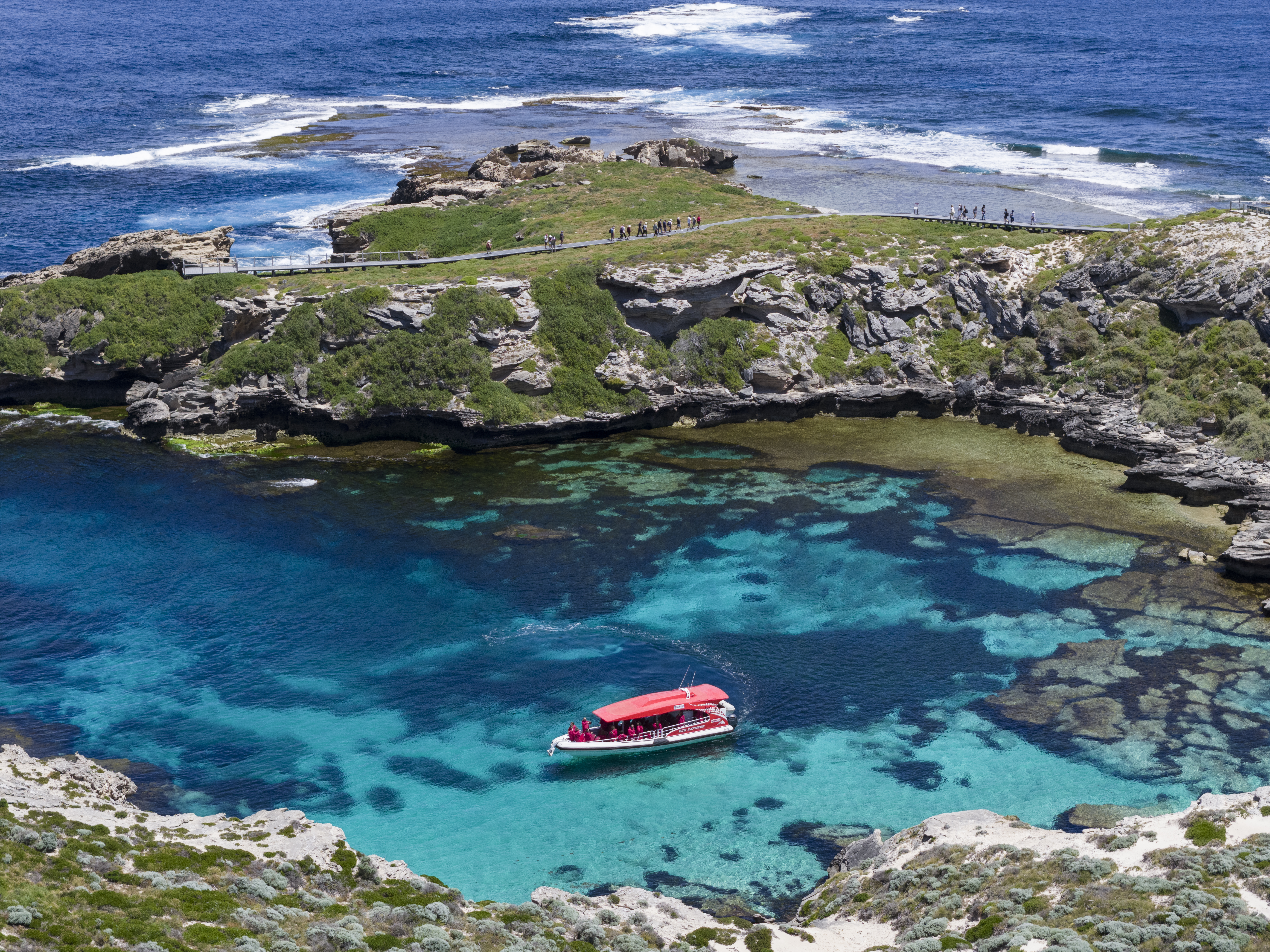 A red and white fast boat sits nestled in a coastal cove surrounded by blue water, and rocky escarpments.
